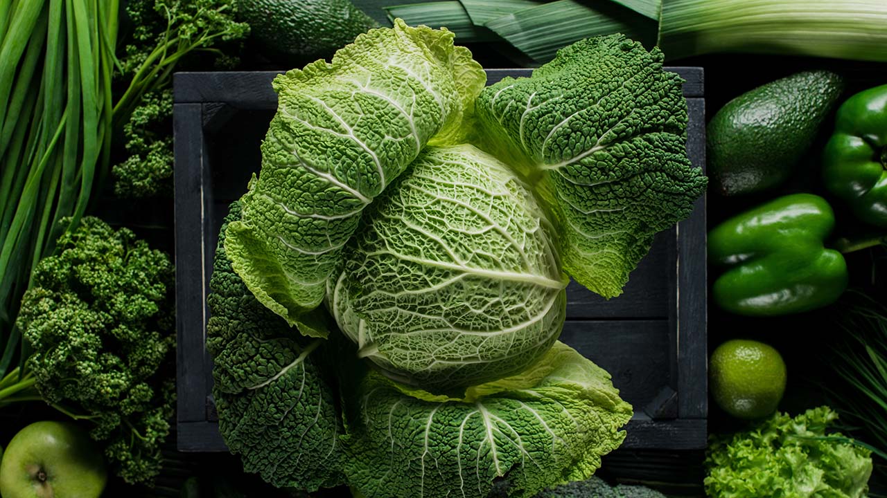 elevated view of green savoy cabbage in wooden box between veget